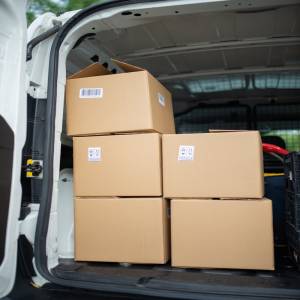 our-story-01 Stacked cardboard boxes inside an open delivery van, ready for shipment.