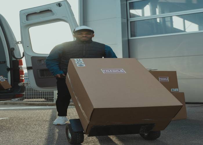 portfolio-05 A delivery man moving cardboard boxes with a trolley outside in daylight.