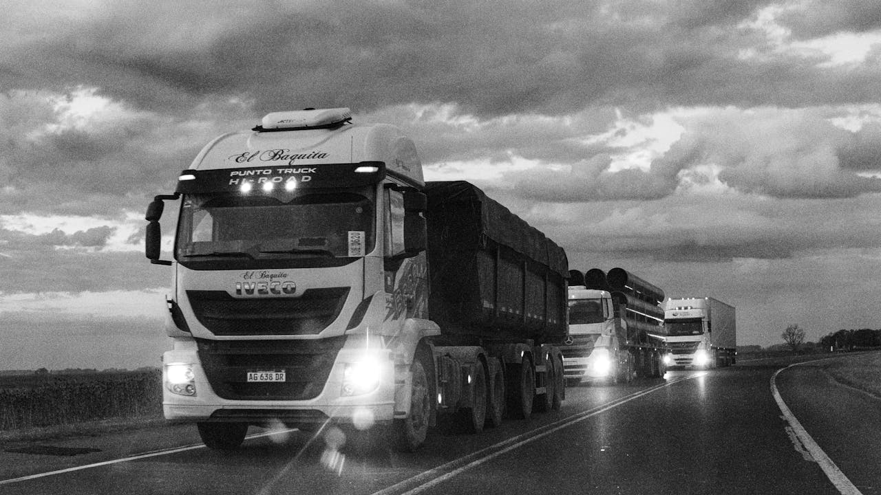 Black and white photo of trucks driving on a highway in Buenos Aires, Argentina at dusk.